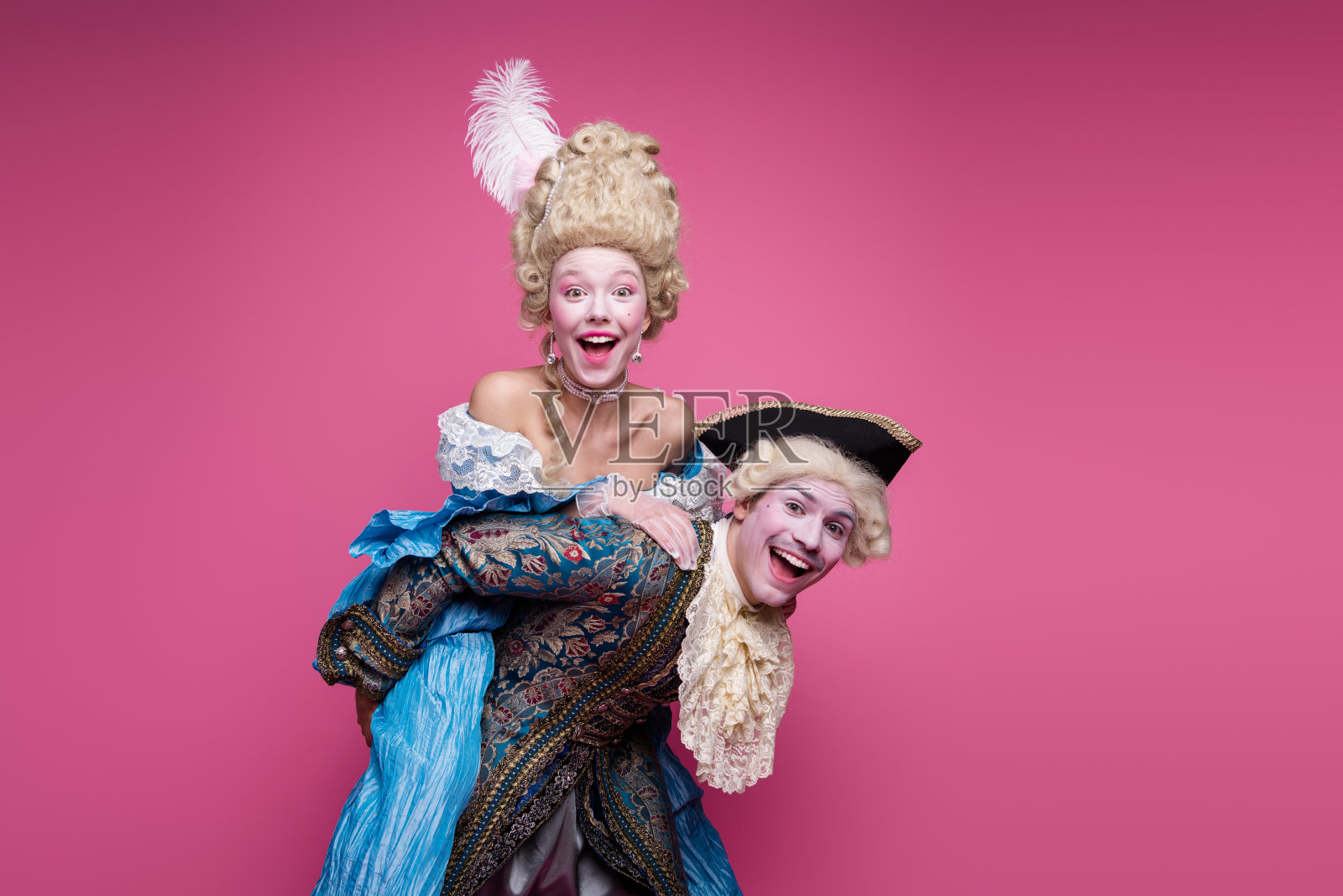 一对快乐的情侣身穿巴洛克风格的服装，在粉色背景前为主题派对摆姿势。男士穿着经典的晚礼服。照片摄影图片