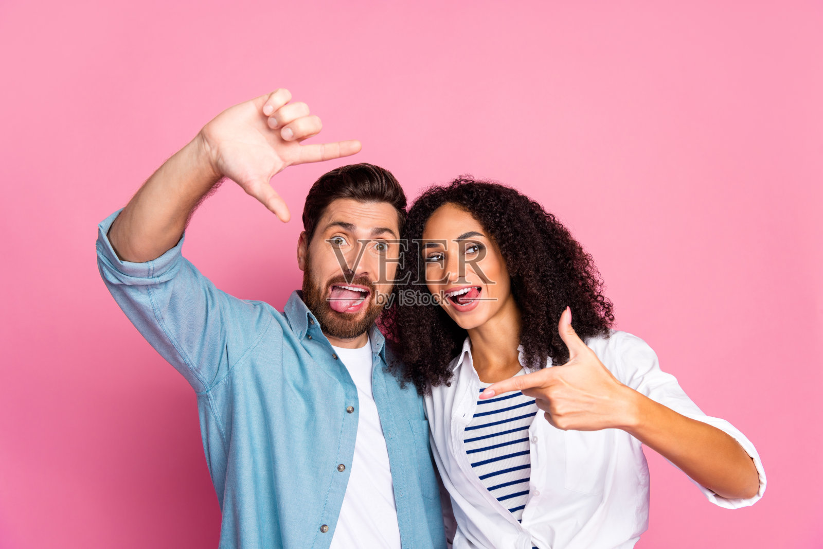 快乐的年轻情侣在明亮的粉色背景前嬉戏摆姿势，表达彼此的爱、乐趣和享受。照片摄影图片