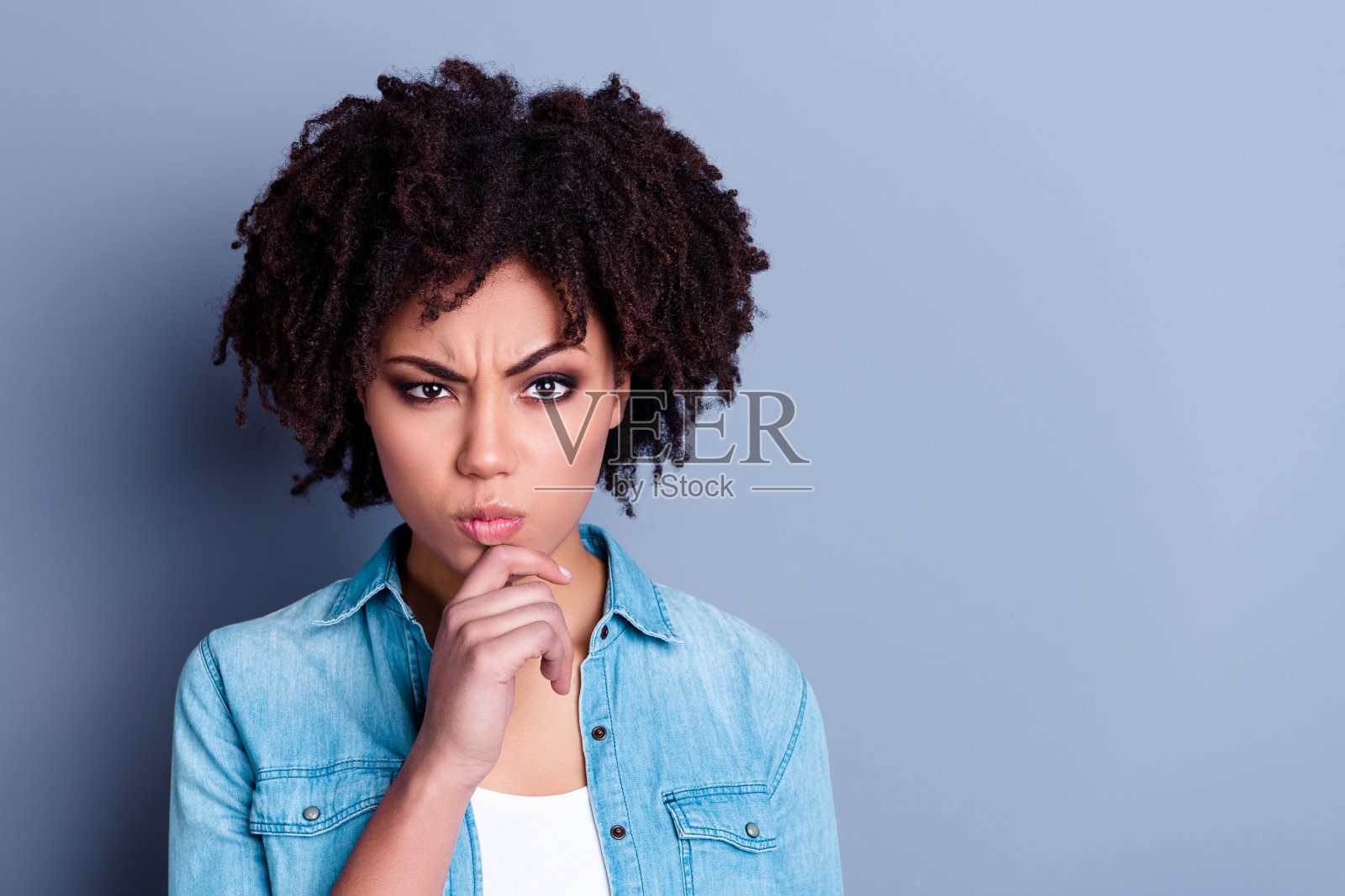 一位聪明的女士手托下巴，目光空洞地凝视着灰色背景，思考选择和决策。照片摄影图片