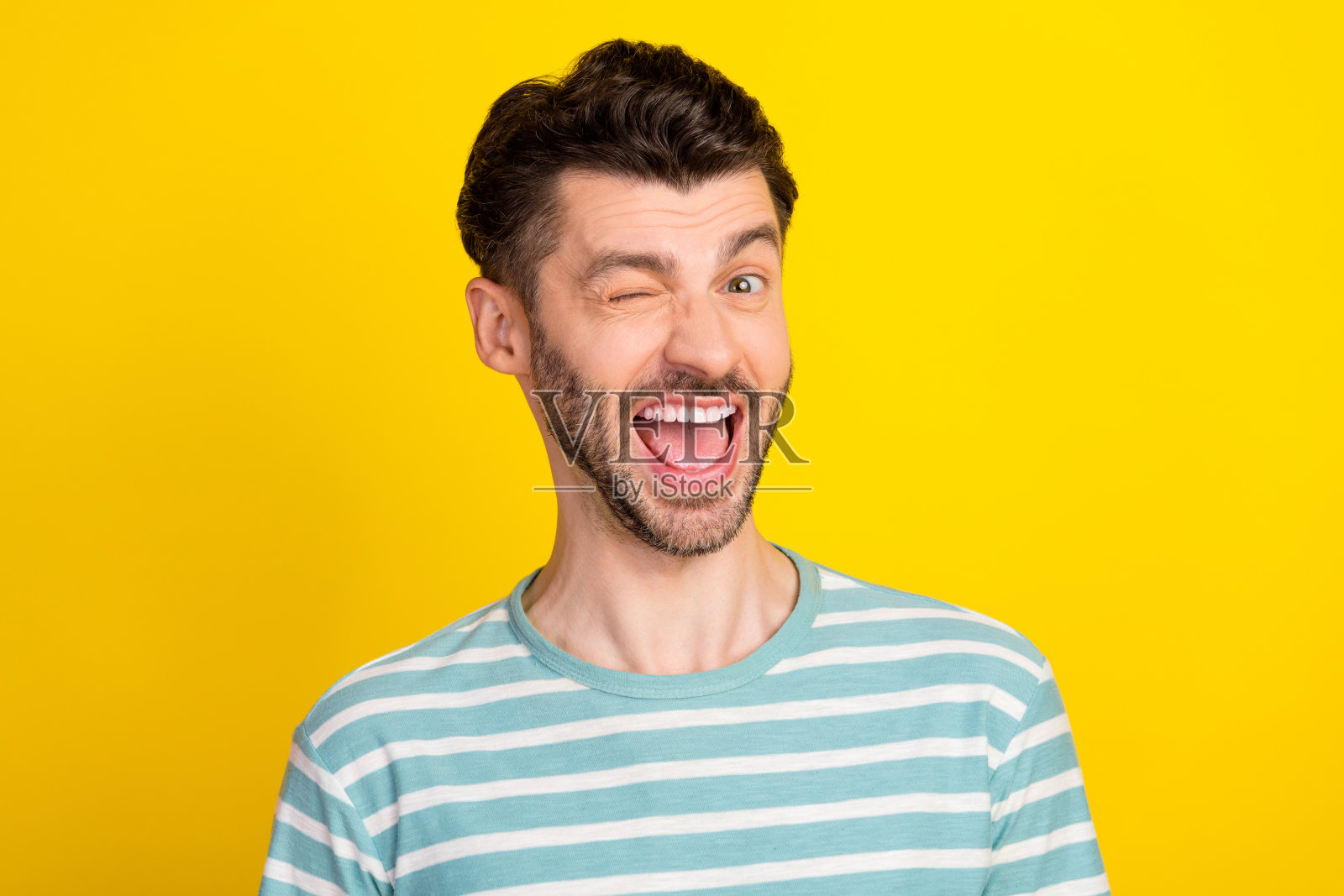 穿着条纹T恤的欢呼男孩在黄色背景上眨眼的照片照片摄影图片