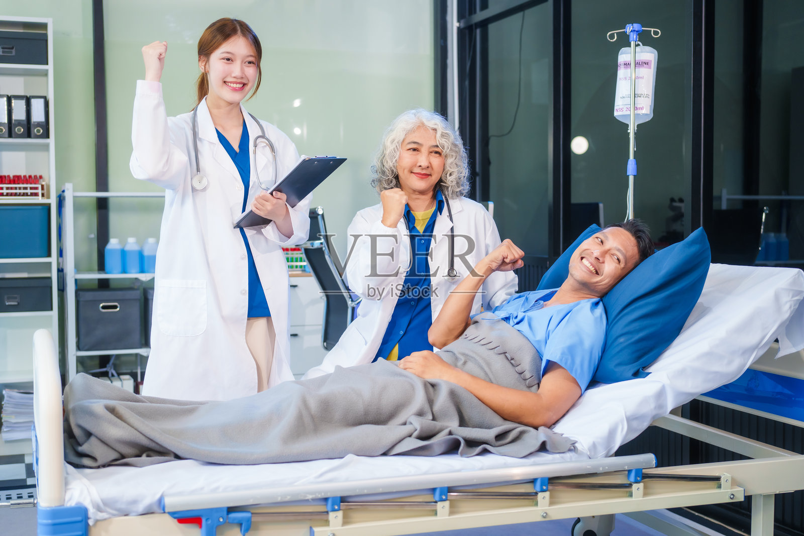 两位女医生在医院病床上检查一名患者，讨论病历，给予药物，并提供鼓励，确保关怀的护理并促进患者的康复。照片摄影图片