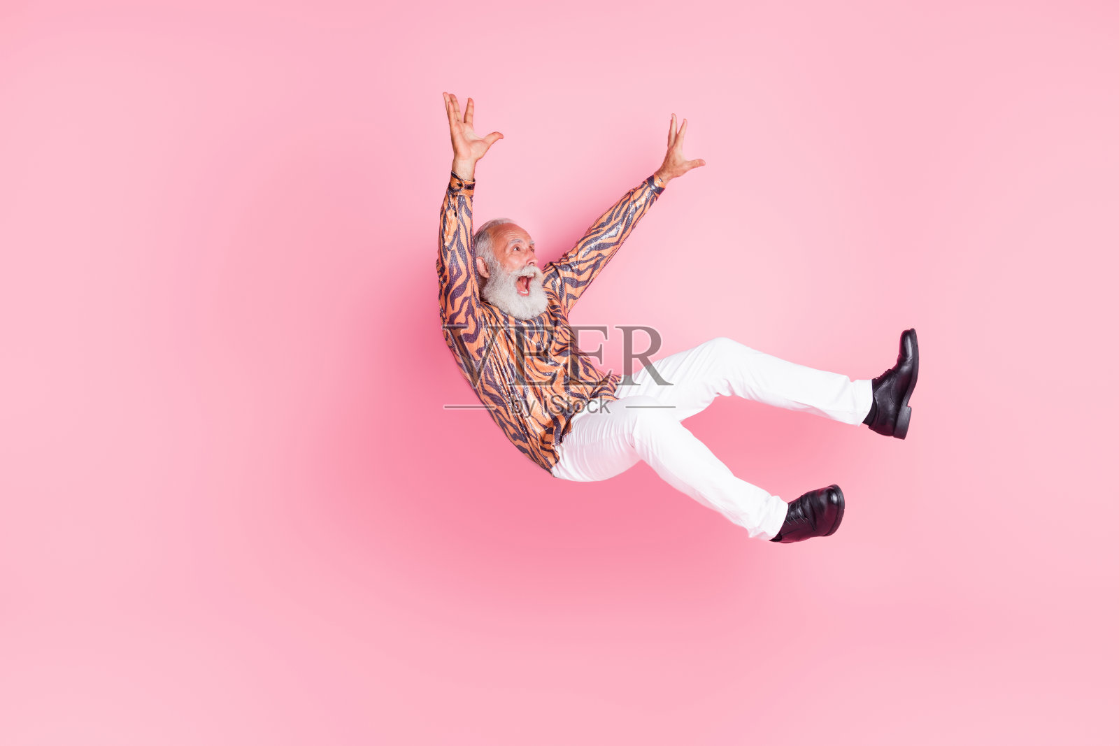 穿着时尚印花衣服的古怪老年男子在粉色背景上飞空跌落。照片摄影图片