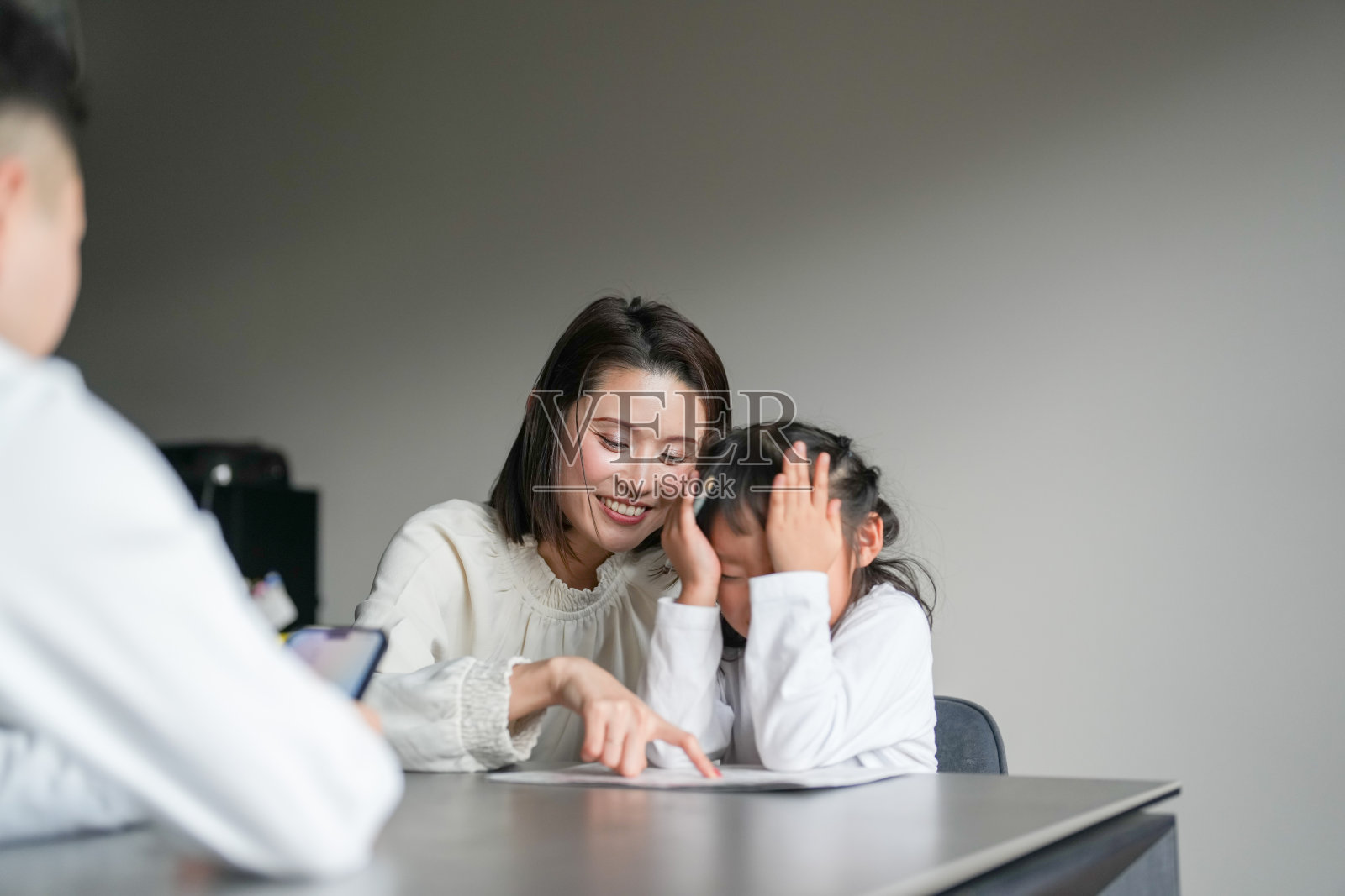 一位30多岁的日本母亲、一位20多岁的父亲和一个6岁的女孩正在客厅的桌子上学习。照片摄影图片