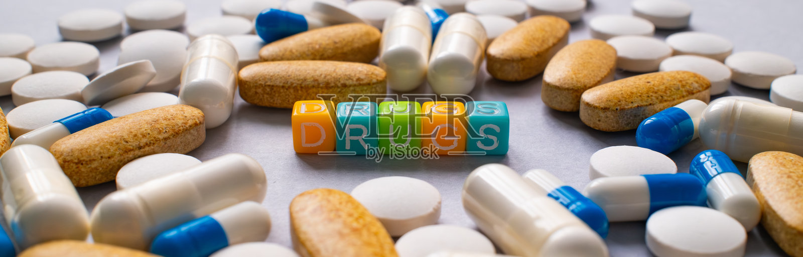 药丸、胶囊和补充剂的排列，中间有五颜六色的方块拼出“DRUGS”这个词。照片摄影图片