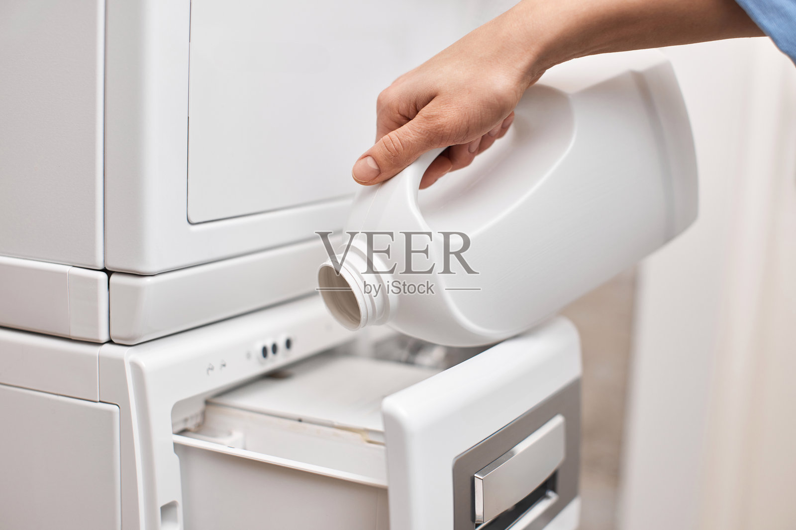 女性手将洗衣液从瓶子倒入洗衣机中照片摄影图片