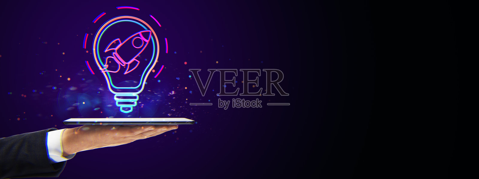 在黑暗背景中，商业人士的手握着平板电脑，灯泡内发光的霓虹火箭象征着创新。照片摄影图片