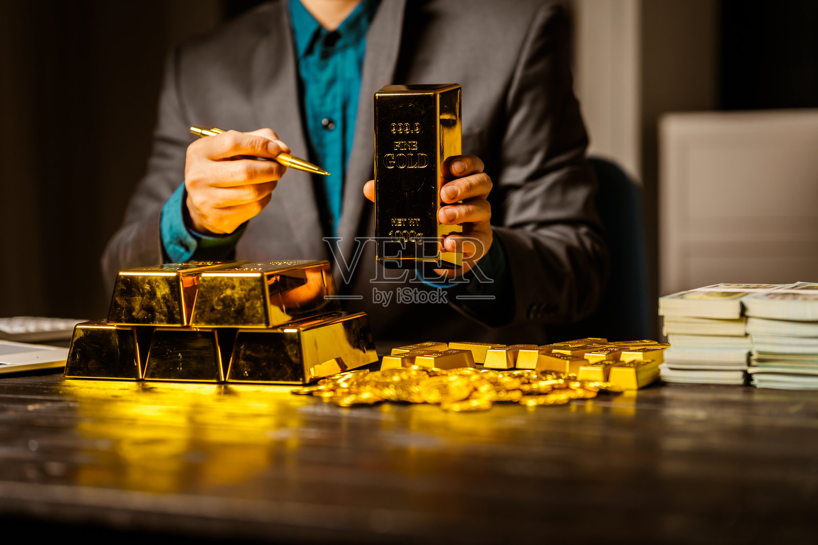 一位商人在夜间办公室的桌子前坐着，使用笔记本电脑分析金条价格、汇率以及黄金交易、采矿和股市的投资计划，面对价格上涨的情况。照片摄影图片