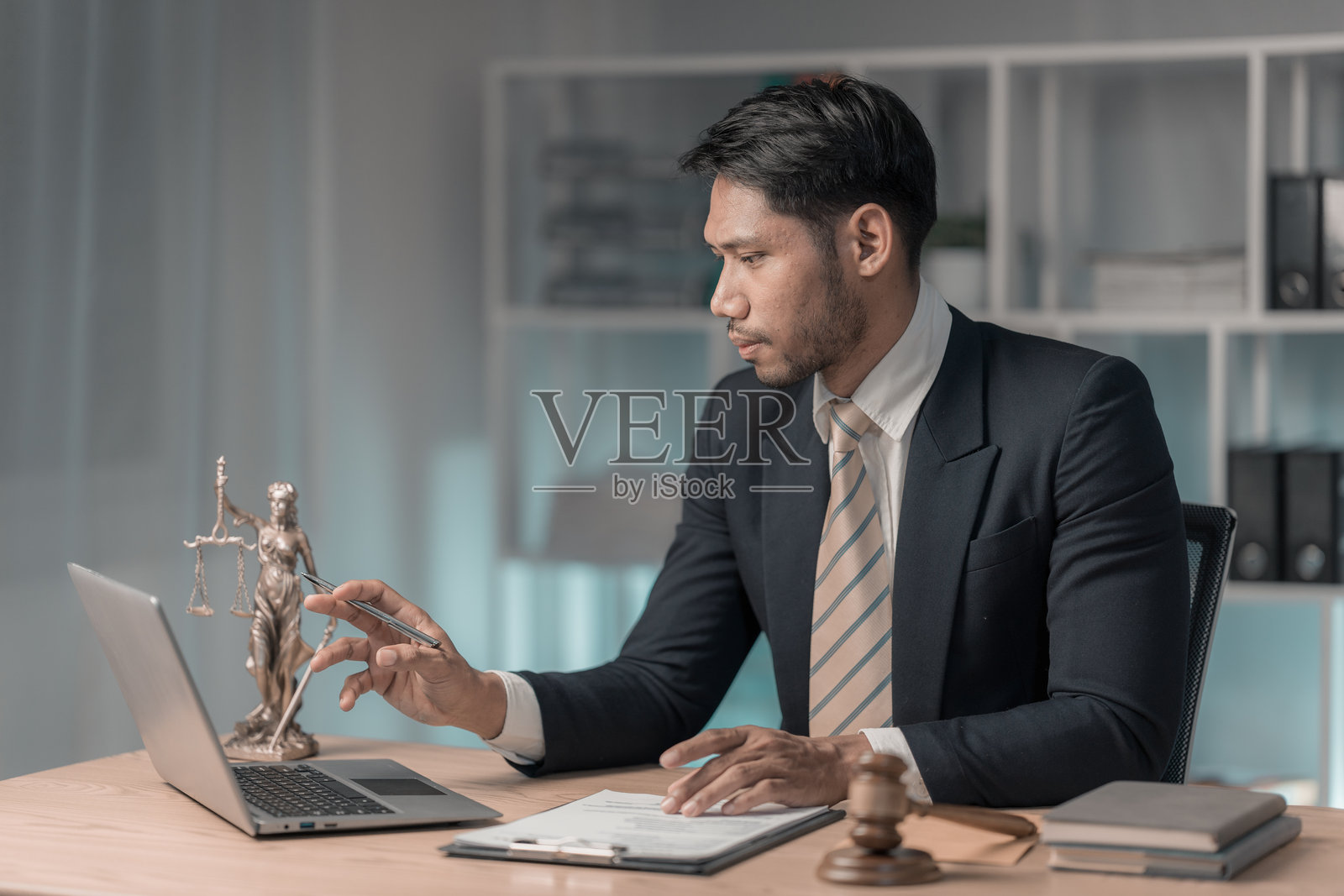 律师在办公室使用笔记本电脑阅读法律书籍，作为法律顾问，涉及司法和法律。男性法官在法庭的木桌上。照片摄影图片