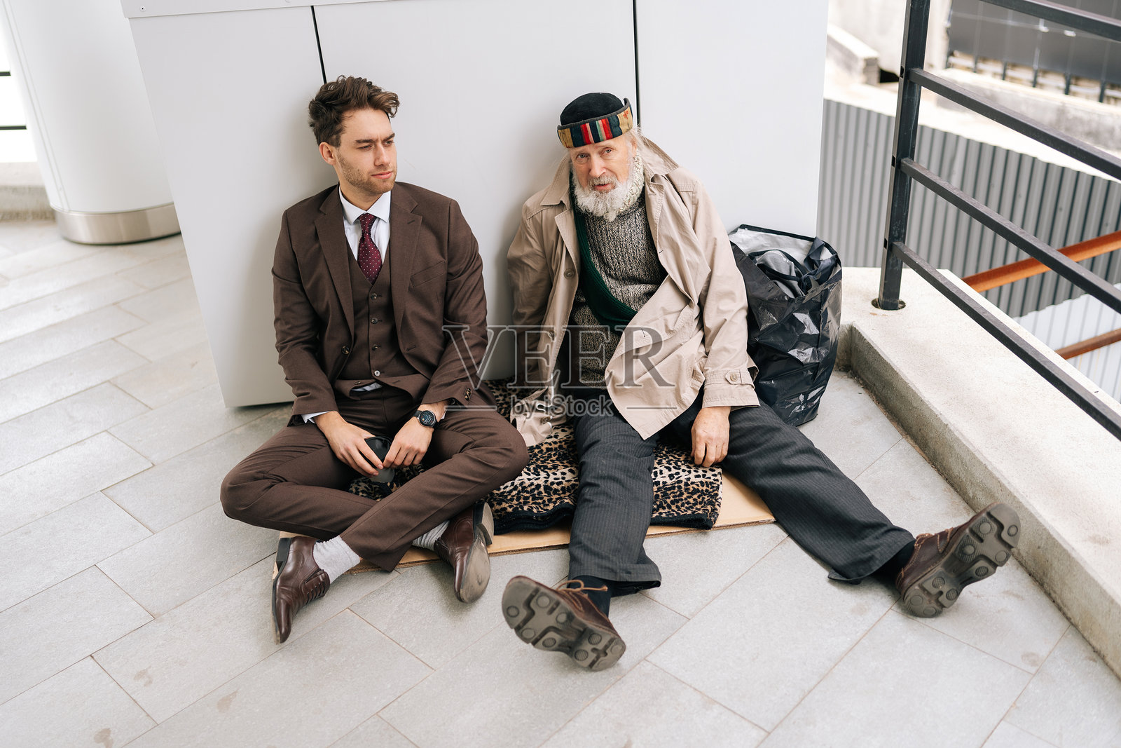 从上方俯视穿着西装的商人与坐在地上纸板上的老年无家可归者，象征着社会不平等和经济差距。照片摄影图片