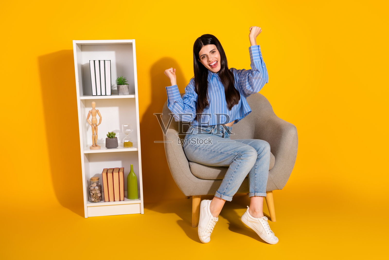 年轻女性坐在椅子上，享受着愉快的时刻，背景是鲜艳的黄色。照片摄影图片