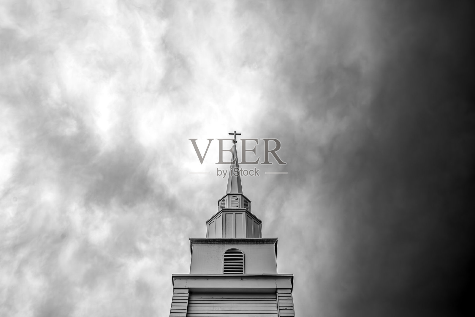 教堂尖塔顶端的十字架在戏剧性的多云天空中高耸。照片摄影图片