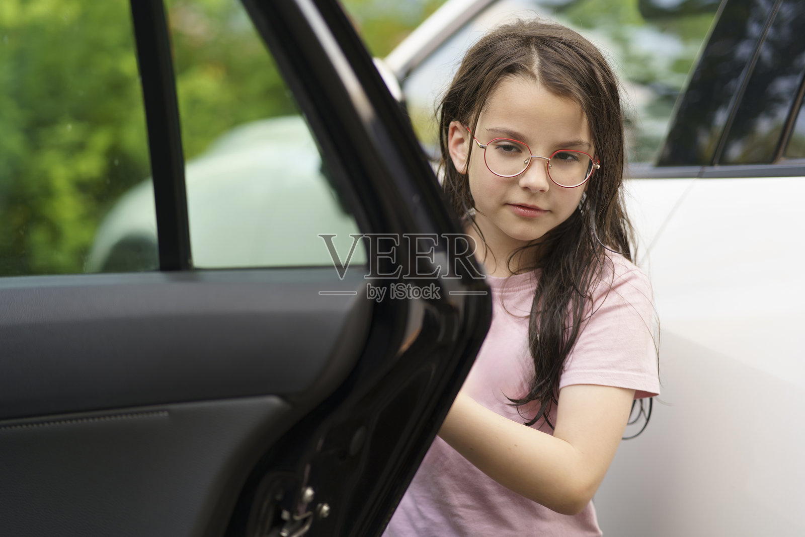 戴眼镜的小女孩穿着T恤，站在停车场旁边打开车门。健康活泼快乐的儿童旅行概念照片摄影图片