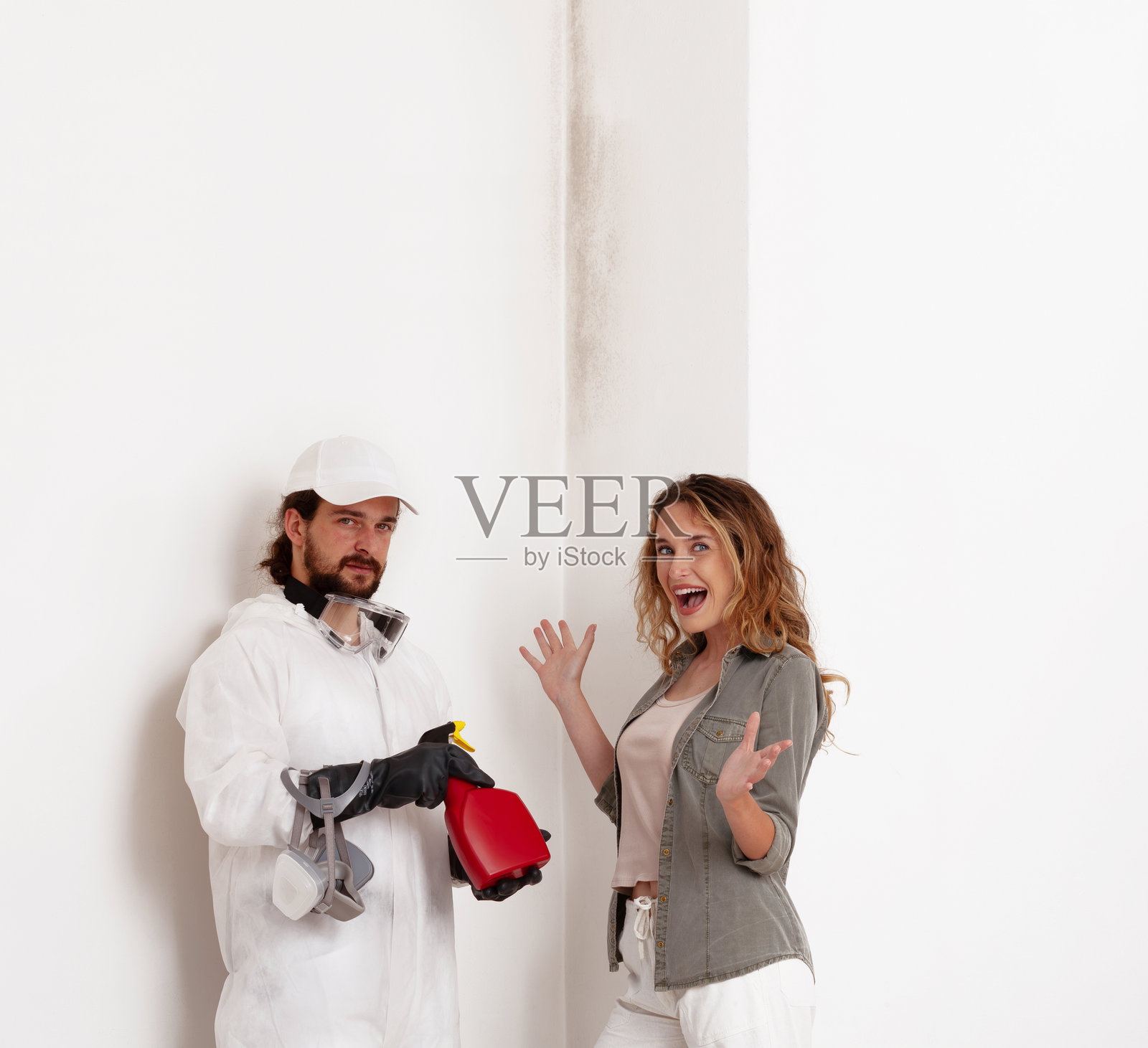 一位专业工作人员在有墙面霉菌问题的家居装修现场向一位开心的女性顾客展示霉菌修复产品。墙面粉刷、清洁和霉菌去除服务的概念。照片摄影图片