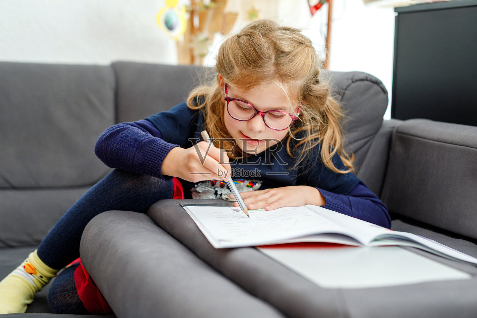 小女孩戴着眼镜在作业本上写字，做学校作业。孩子用铅笔练习写数字，专注于学习。小学，教育。照片摄影图片