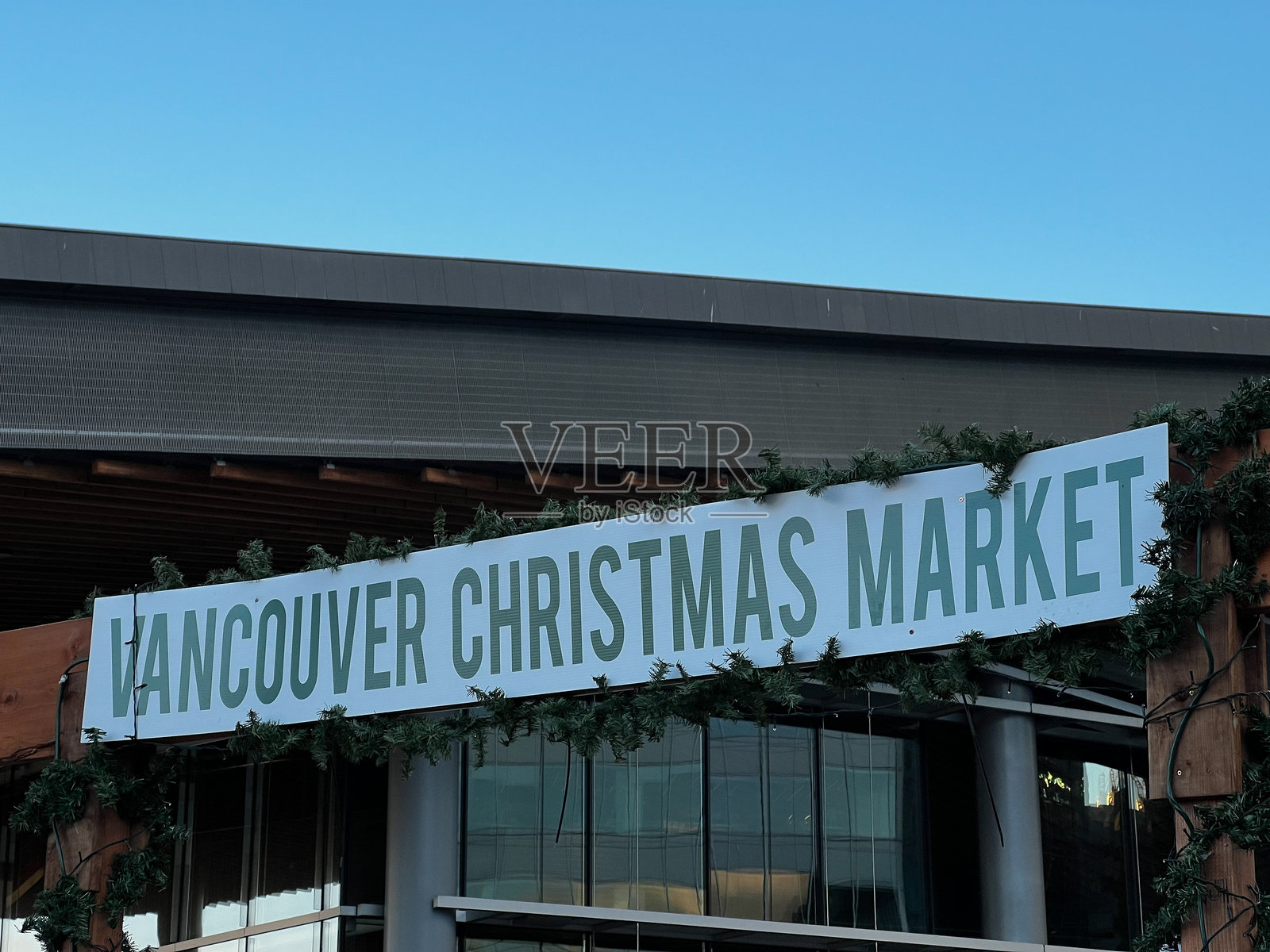 大型标牌上写着“温哥华圣诞市场”，背景是现代建筑外立面，装饰有常青藤花环，蓝天映衬。照片摄影图片
