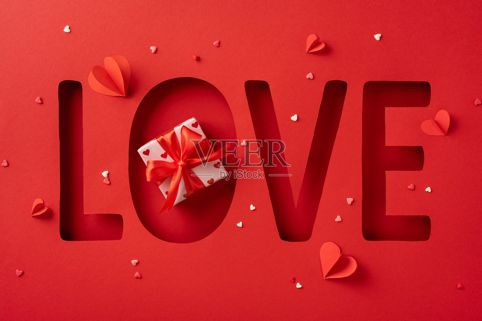 一个以红色为主题的情人节图像，字母“O”里面有一个礼物盒，周围环绕着心形装饰，字样为“LOVE”。照片摄影图片