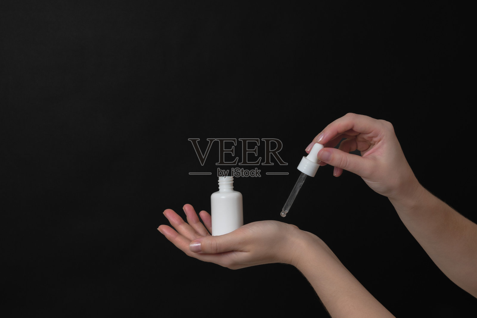 手握玻璃瓶的精华液或带滴管的精油，背景为黑色。自然有机水疗美容概念照片摄影图片