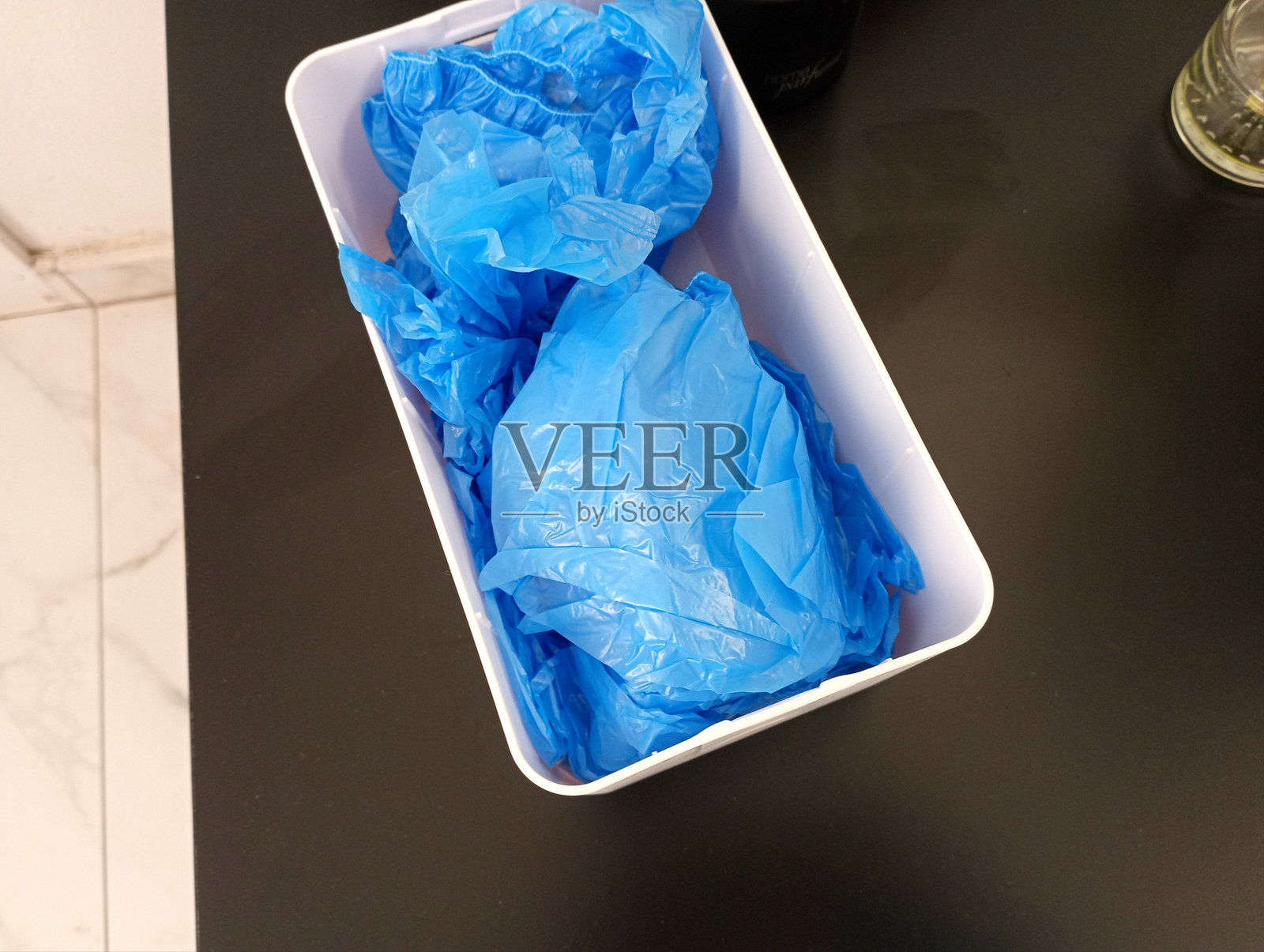 医生办公室桌子上的塑料容器，里面装有蓝色聚乙烯鞋套。照片摄影图片