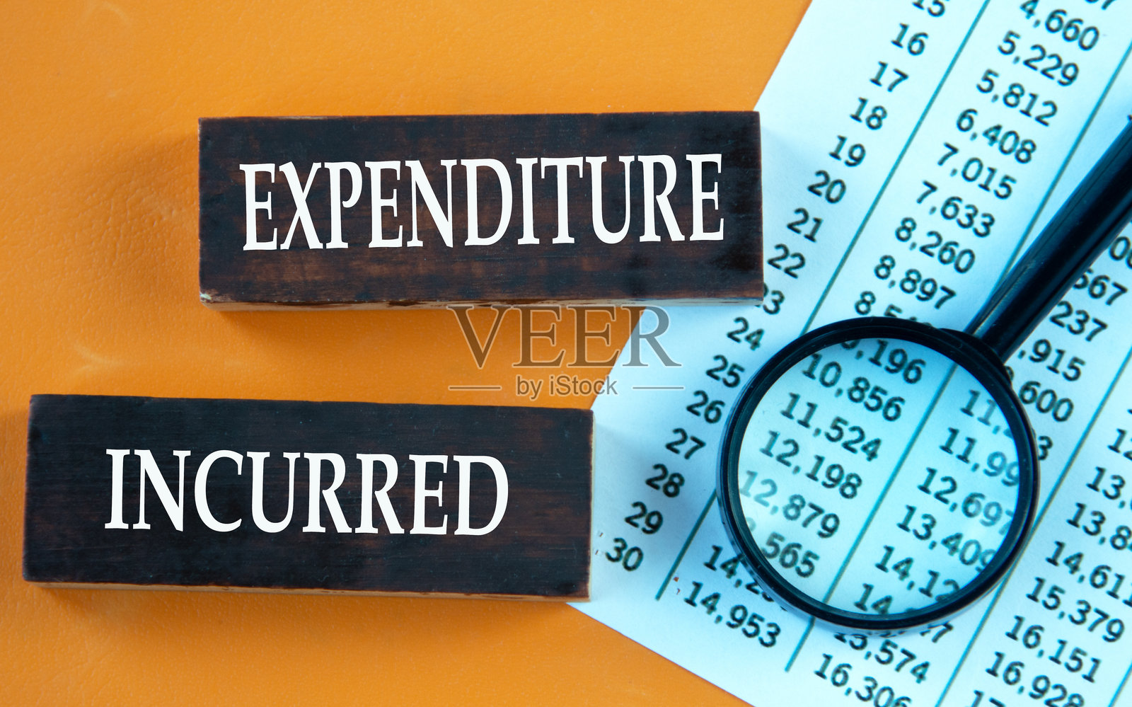 支出发生 - 在放大镜和数字表背景下的棕色木条上的文字照片摄影图片