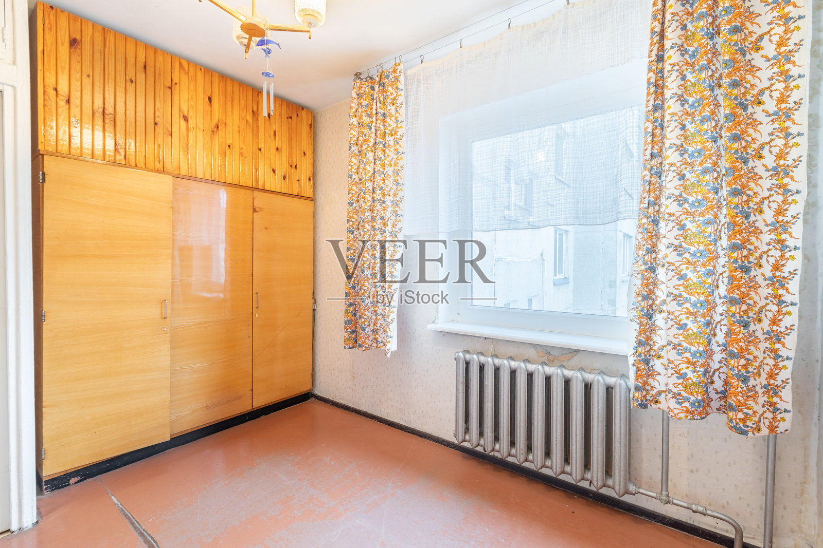 简单的房间室内，配有木质衣柜和阳光明媚的窗户。明亮的老式复古房间室内，配有光辉的窗帘和自然光。旧壁纸，复古加热器，散热器。照片摄影图片