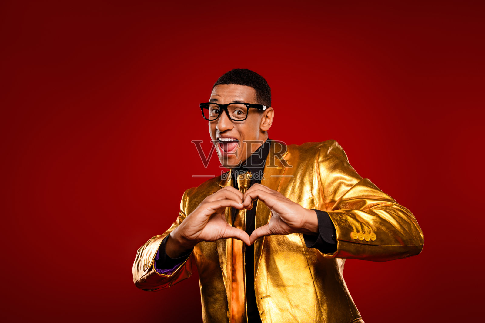 身穿金色西装的迷人年轻男子在鲜艳的红色背景前做出心形手势，象征着爱。照片摄影图片