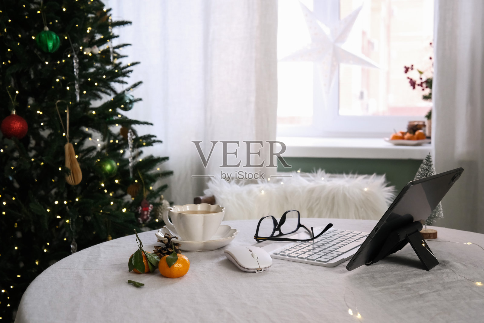 一个舒适的家庭办公室布置，配有平板电脑、键盘、节日装饰和温暖的饮品，以提升氛围照片摄影图片