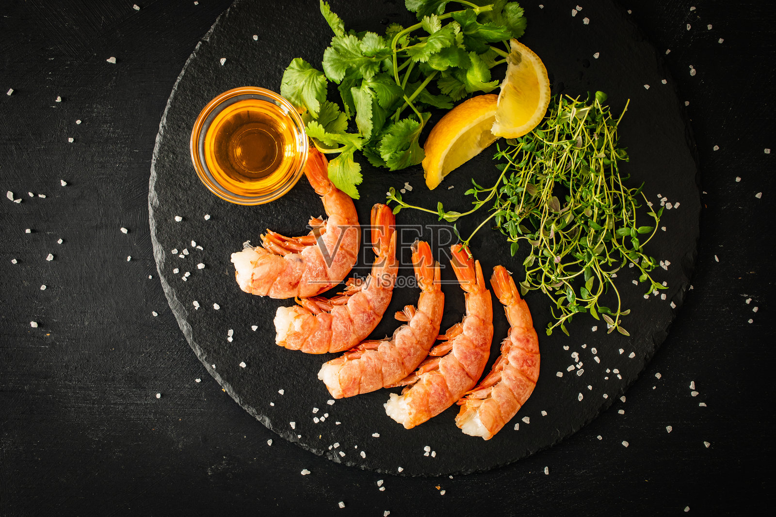 用百里香、柠檬和香菜准备的生虾放在黑色石板上照片摄影图片