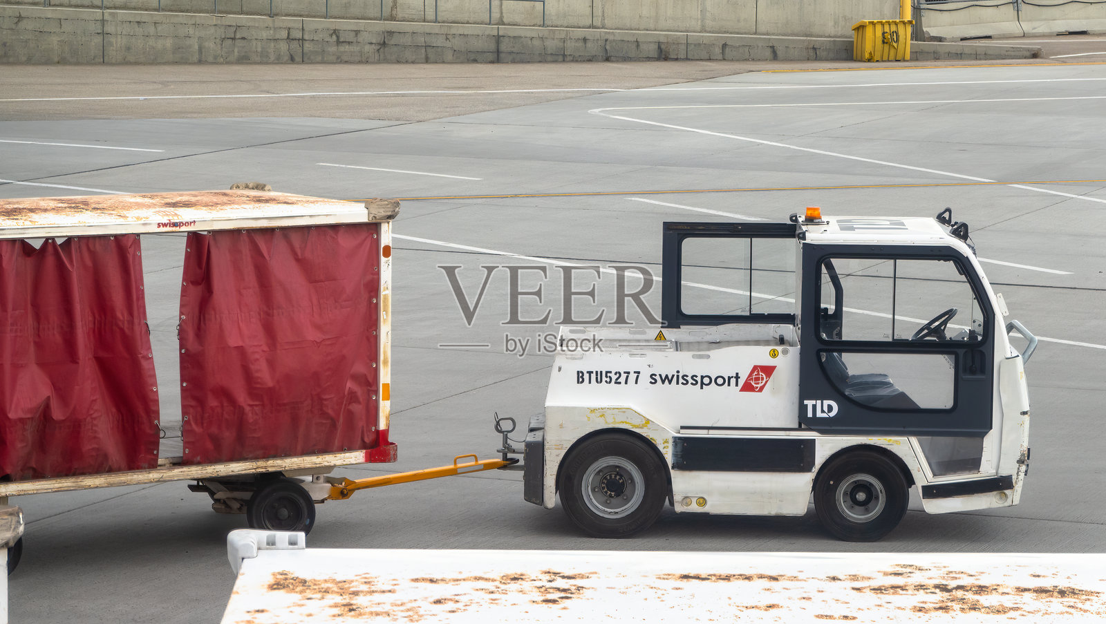 一辆标有Swissport TLD的行李拖车正在机场停机坪上移动行李车。照片摄影图片