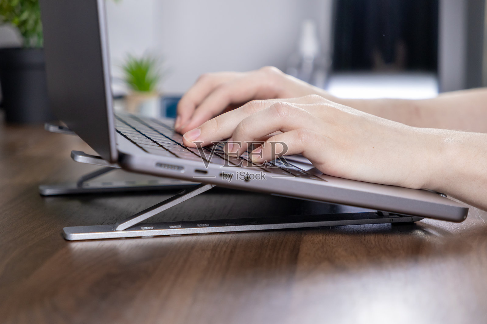 在整洁有序的工作空间中，手在木桌上使用带有人体工学支架的笔记本电脑打字，以改善姿势。照片摄影图片
