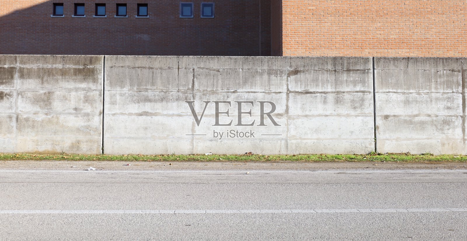 路边的粗糙混凝土围墙，后面是砖墙外观。前方是道路。照片摄影图片