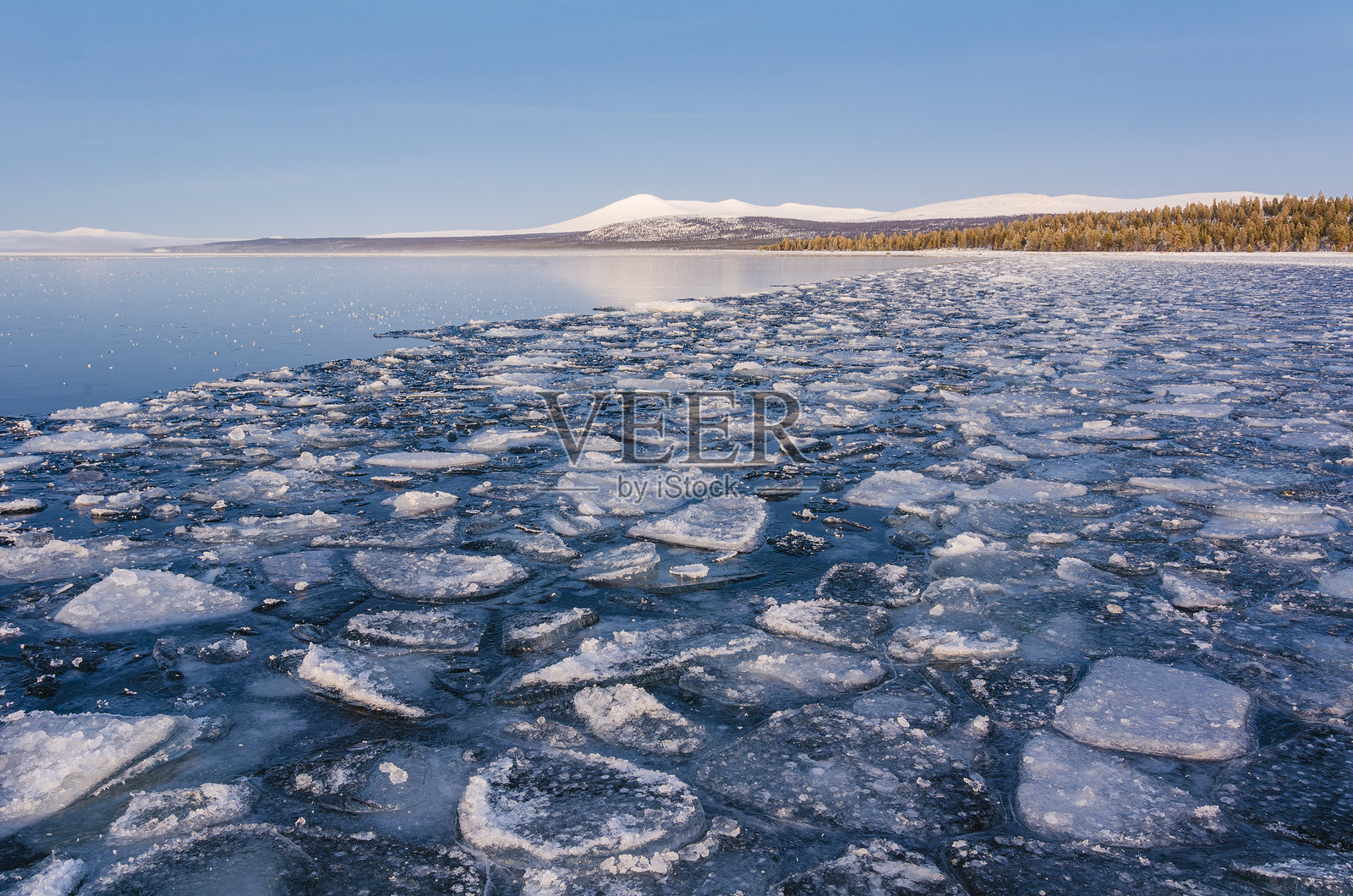 宁静的冬季风景中，冰湖上漂浮着冰块，远处是雪山。照片摄影图片