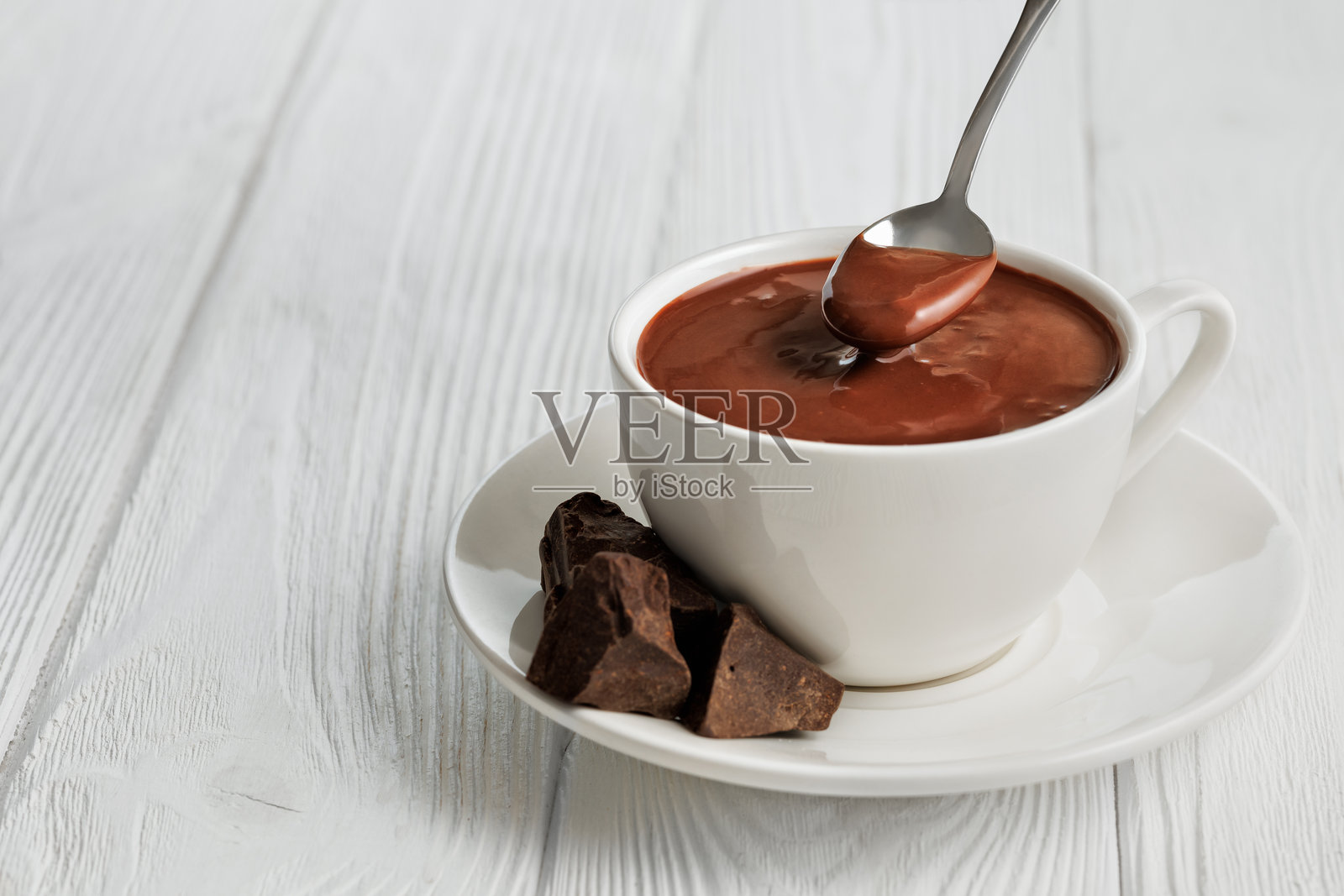 白色木桌上的杯子和勺子里的热巧克力照片摄影图片