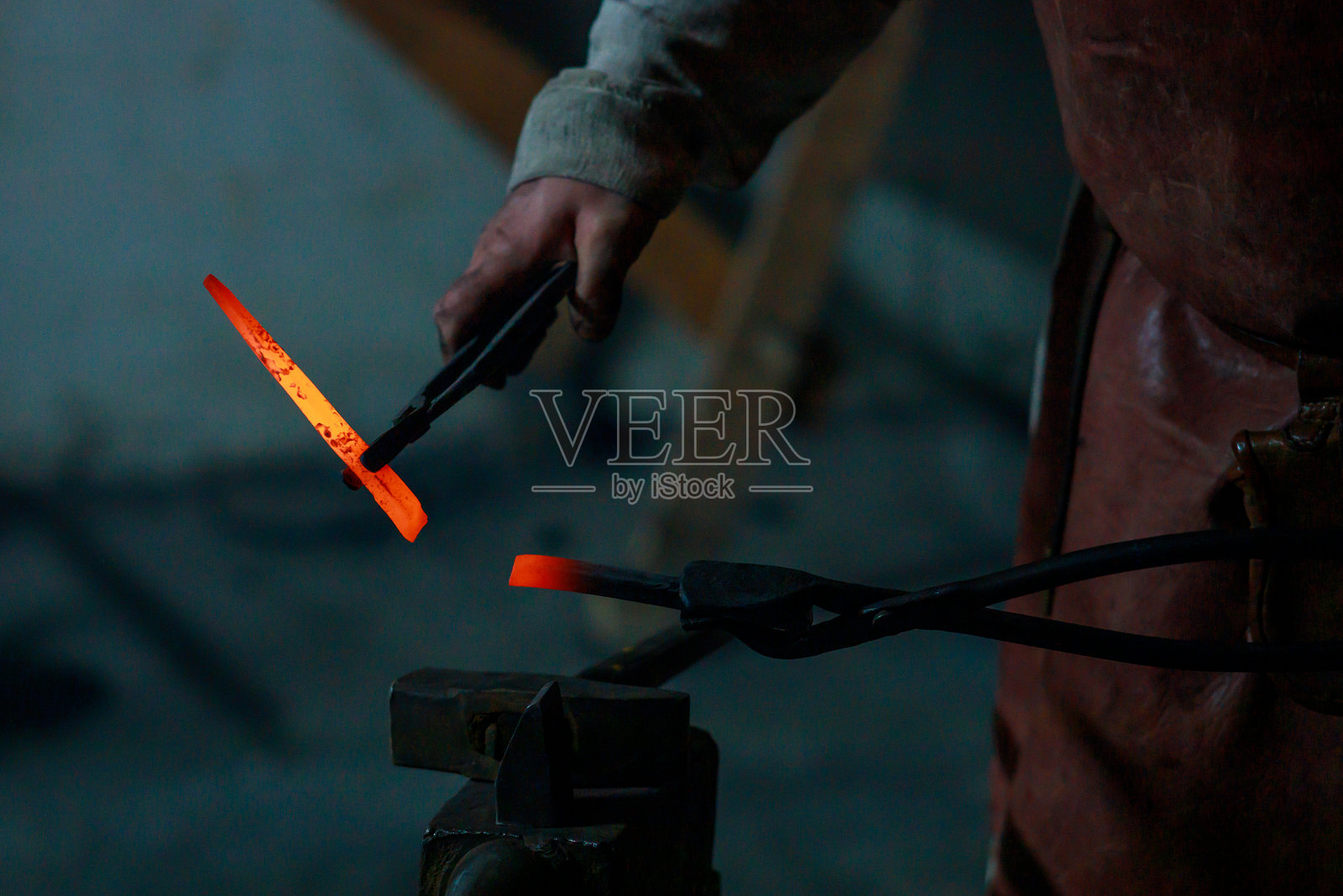 一个男人正用钳子夹住一块发红的金属。照片摄影图片