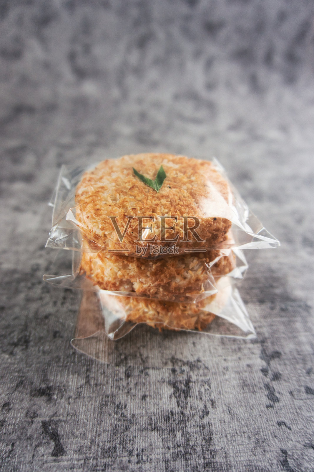 灰色背景上三块椰子饼的特写，包装在塑料袋中。Sagon是一种典型的印尼蛋糕，由糯米粉和椰子丝制成。照片摄影图片