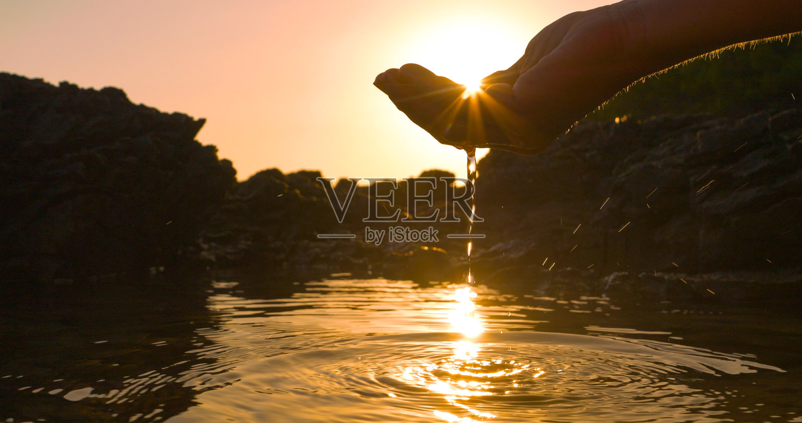 特写，镜头光晕：阳光透过手掌舀起的海水洼中的水面。照片摄影图片