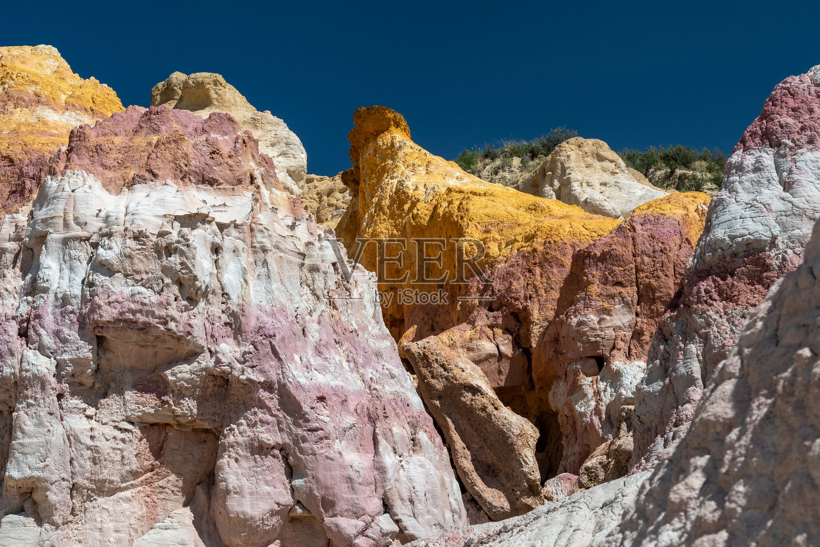 在阳光明媚的正午，五彩斑斓的岩石形成在崎岖的地形中，沙质悬崖映衬出充满活力的沙漠景观。照片摄影图片