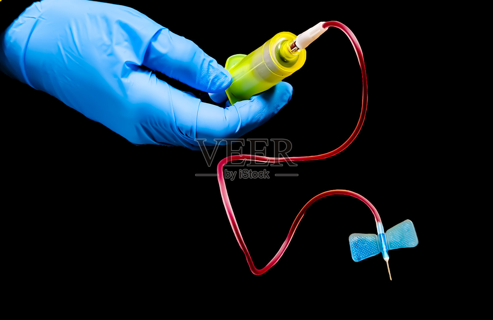 一只戴着手套的手在黑色背景下握着一根蝴蝶针，蝴蝶针是一种用于抽血或输注静脉液体的医疗设备。照片摄影图片