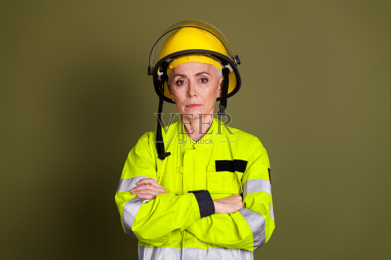 成熟的女消防员穿着高可视性的防护工作服和头盔，背景为卡其色照片摄影图片