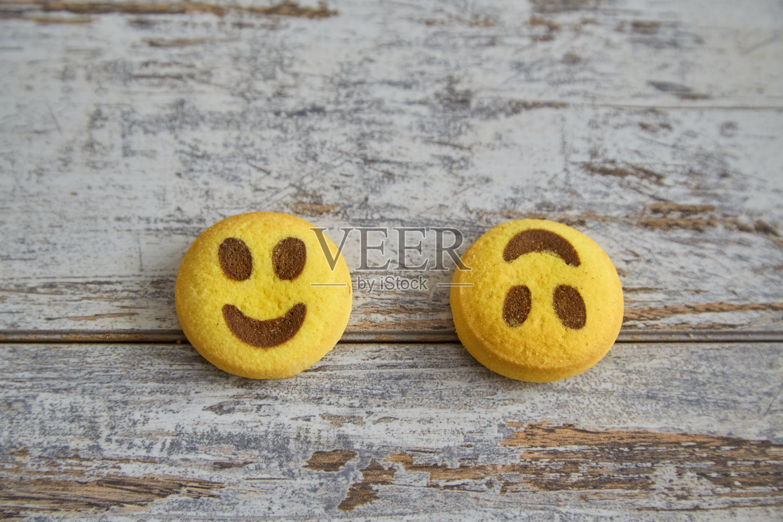 黄色饼干呈微笑表情和倒置微笑表情，靠在一起放在木桌上，特写，悲伤与快乐并存。照片摄影图片