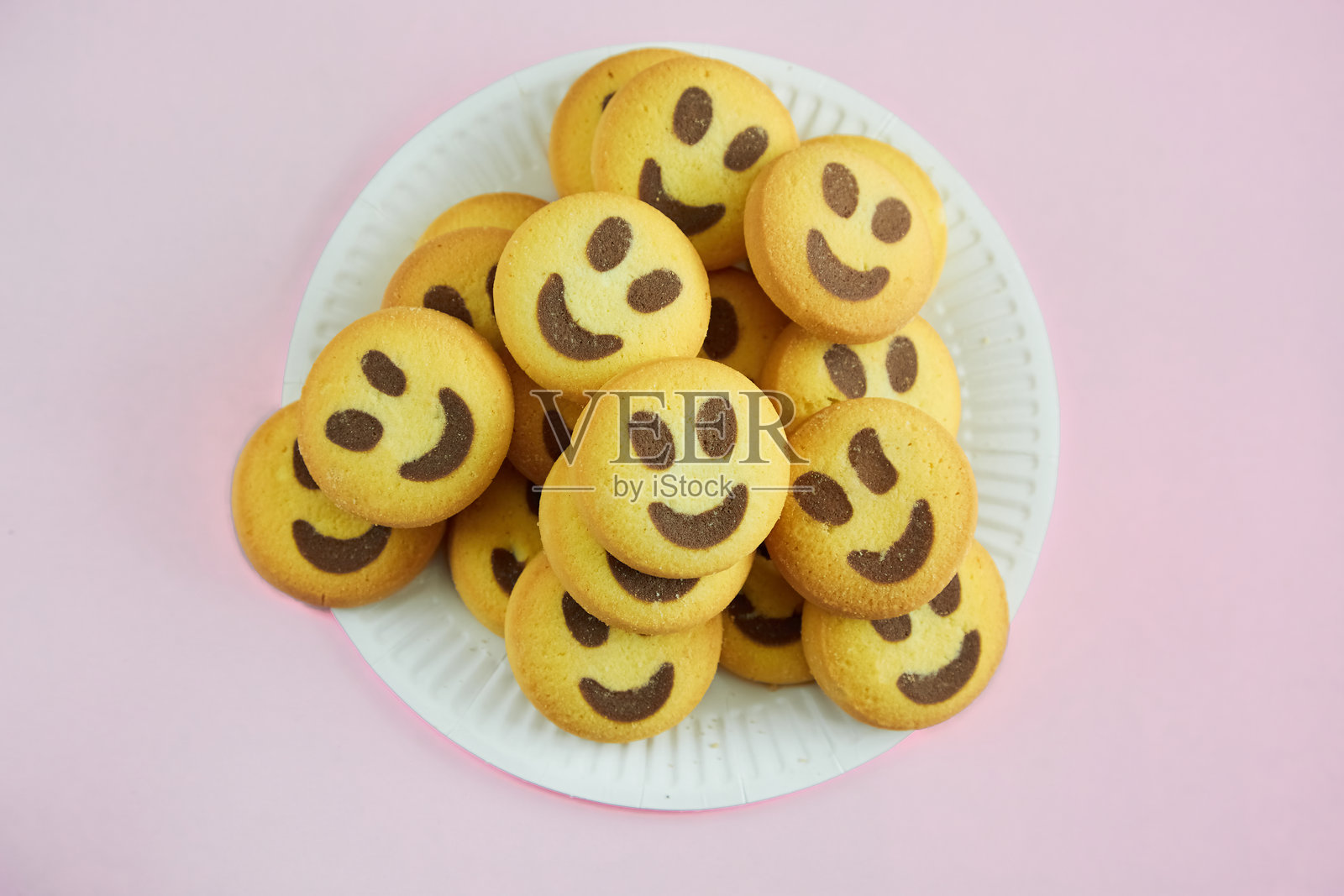 微笑饼干堆放在白色纸盘上，背景为粉色，传达和谐与理解，家庭的温馨，愉快的问候，美味的食谱。照片摄影图片