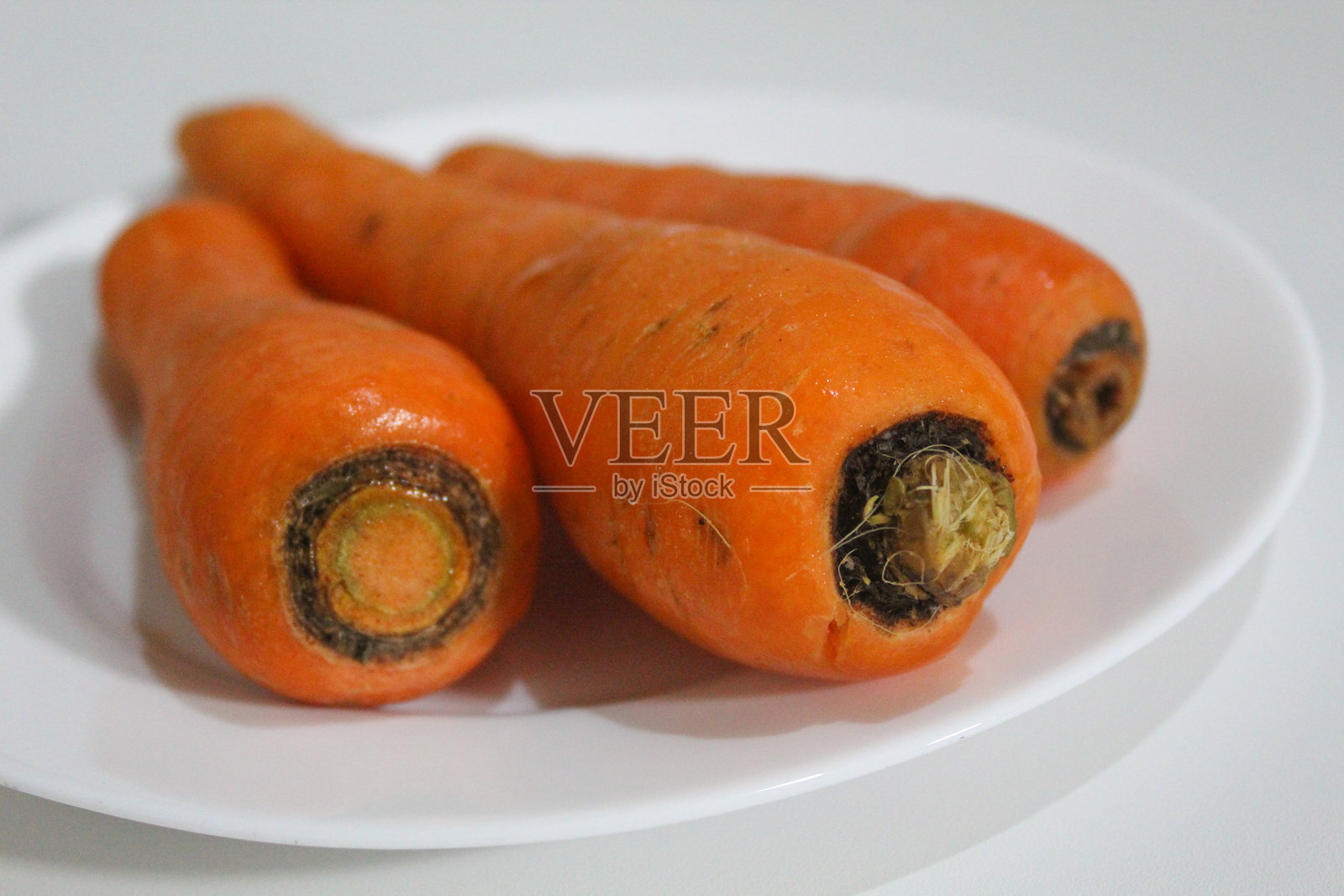 三根胡萝卜放在白色盘子上，背景为白色。新鲜的胡萝卜，未去皮，未烹饪。照片摄影图片