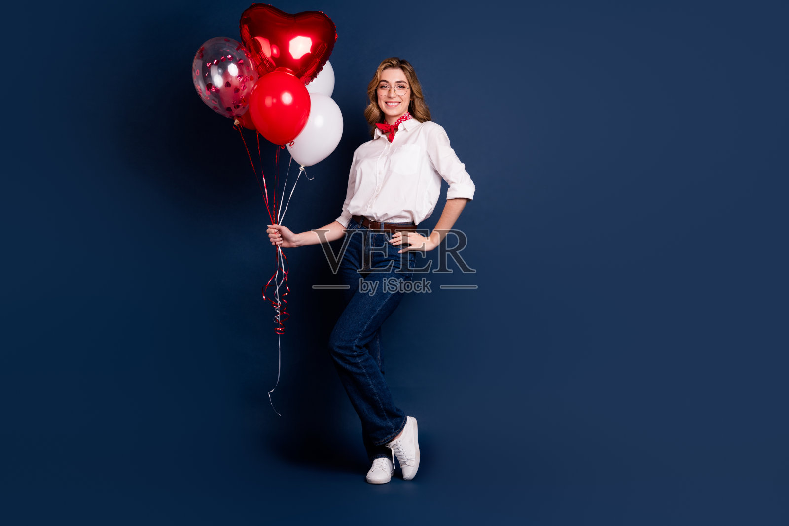 时尚的年轻女性穿着休闲服，手持色彩鲜艳的气球，背景为深蓝色，适合节日庆祝。照片摄影图片