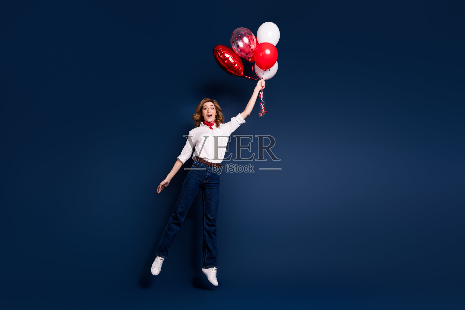 身穿白衬衫的年轻女性在深蓝色背景前以时尚姿势手持节日气球照片摄影图片
