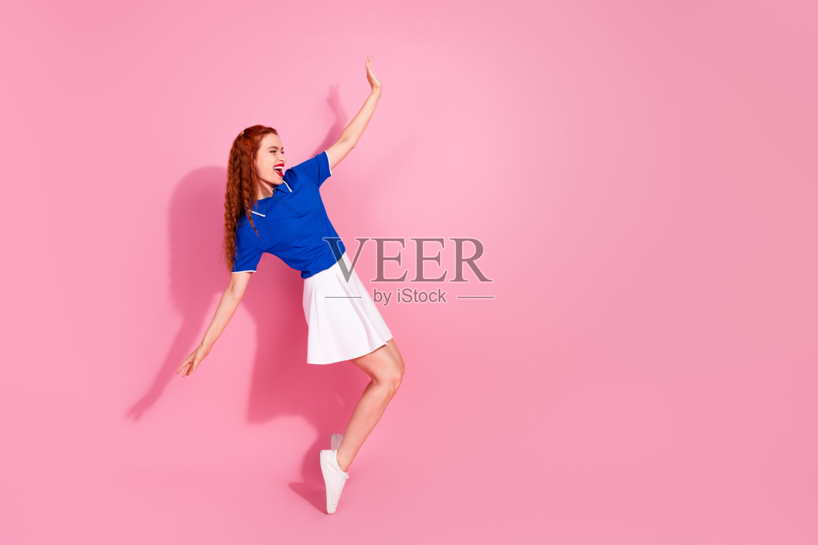 全身照，光鲜迷人的女士穿着迷你裙，在粉色背景的空旷空间中尽情玩乐。照片摄影图片