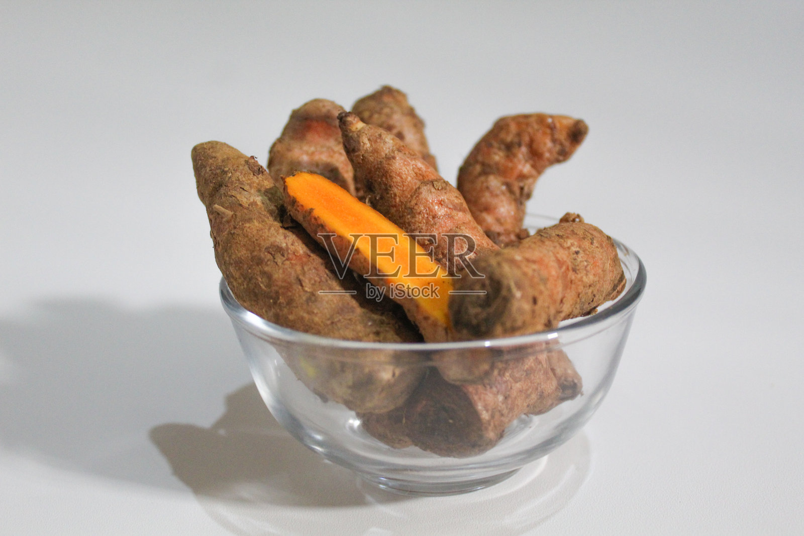 碗中的姜黄或黄姜根茎，背景为白色。完整的块状和去皮的块状，肉质清晰可见。照片摄影图片