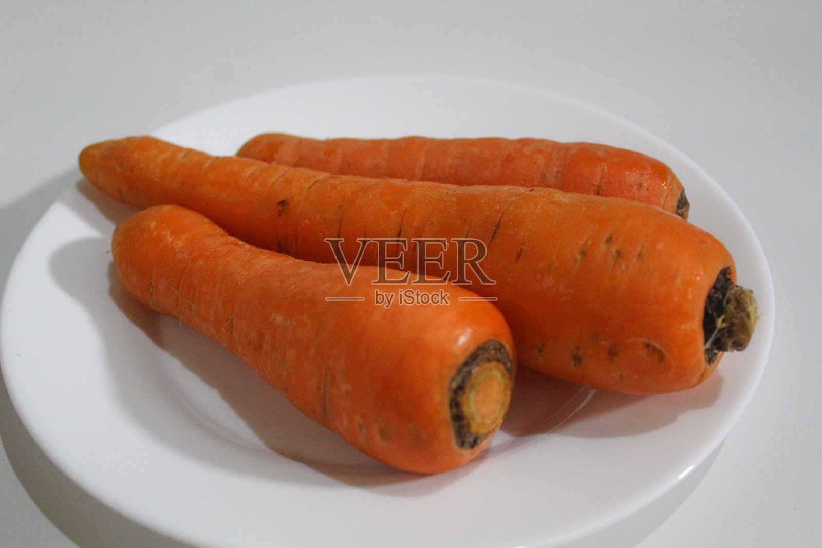 三根胡萝卜放在白色盘子上，背景为白色。新鲜的胡萝卜，未去皮，未烹饪。照片摄影图片