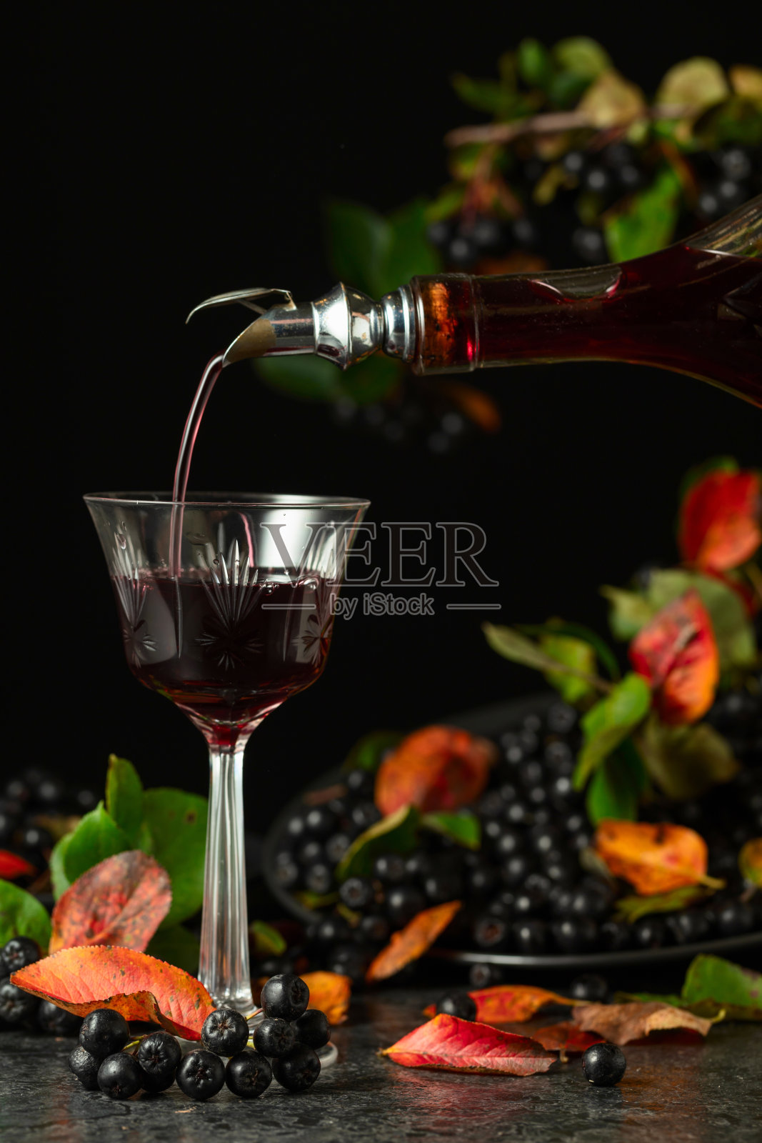 黑果枸杞利口酒从瓶中倒入玻璃杯。照片摄影图片