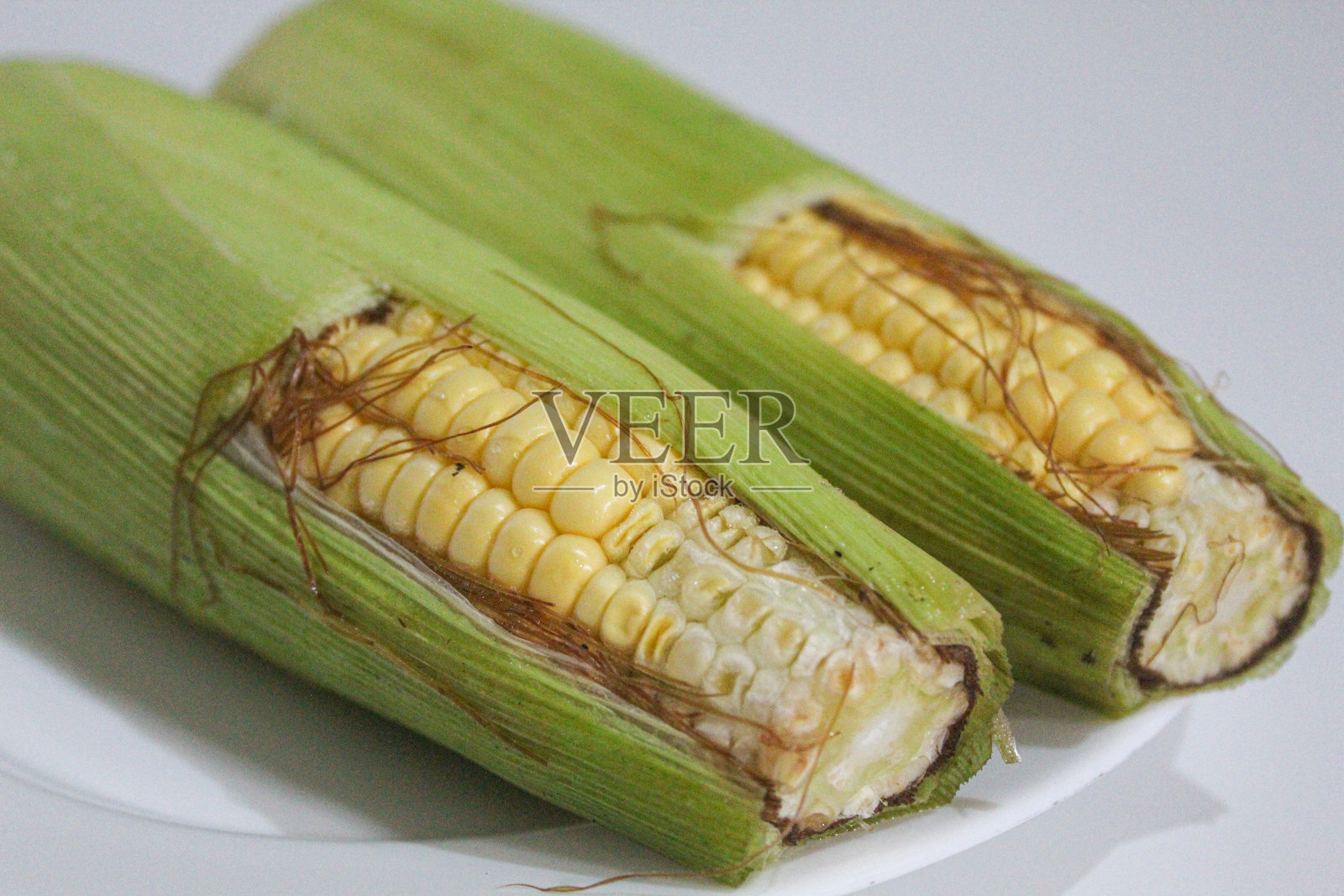 两颗带有绿色外壳和棕色丝须的黄色玉米粒，孤立在白色背景上照片摄影图片