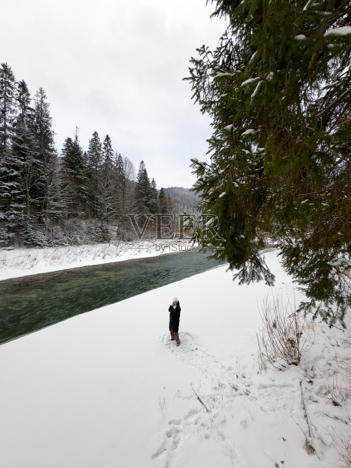 雪-covered河岸上的人，背景是森林和桥梁照片摄影图片