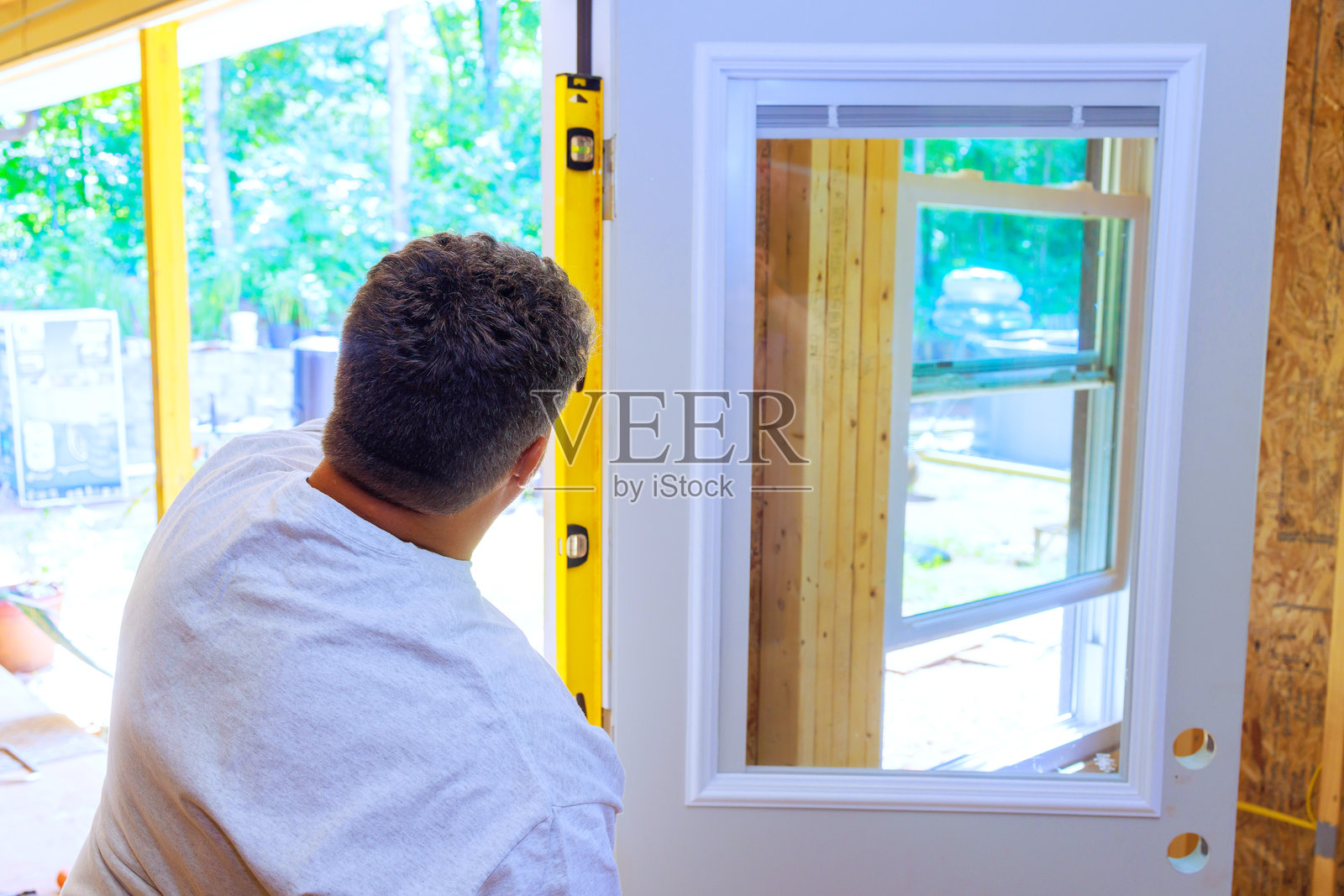 在新房子安装前门时，一位木匠使用黄色的水平尺。照片摄影图片